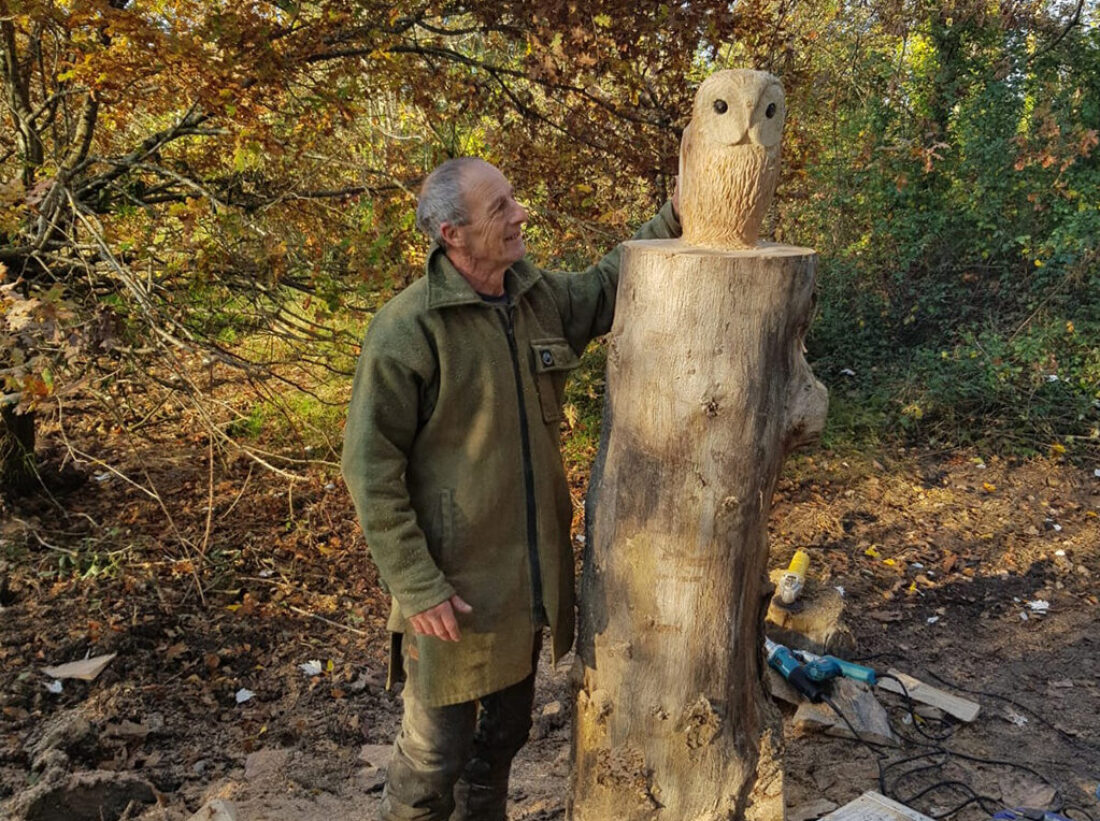 A man stood next to an owl carved into a tree trunk