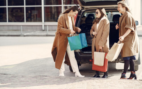 Three women with shopping bags stood by a car boot