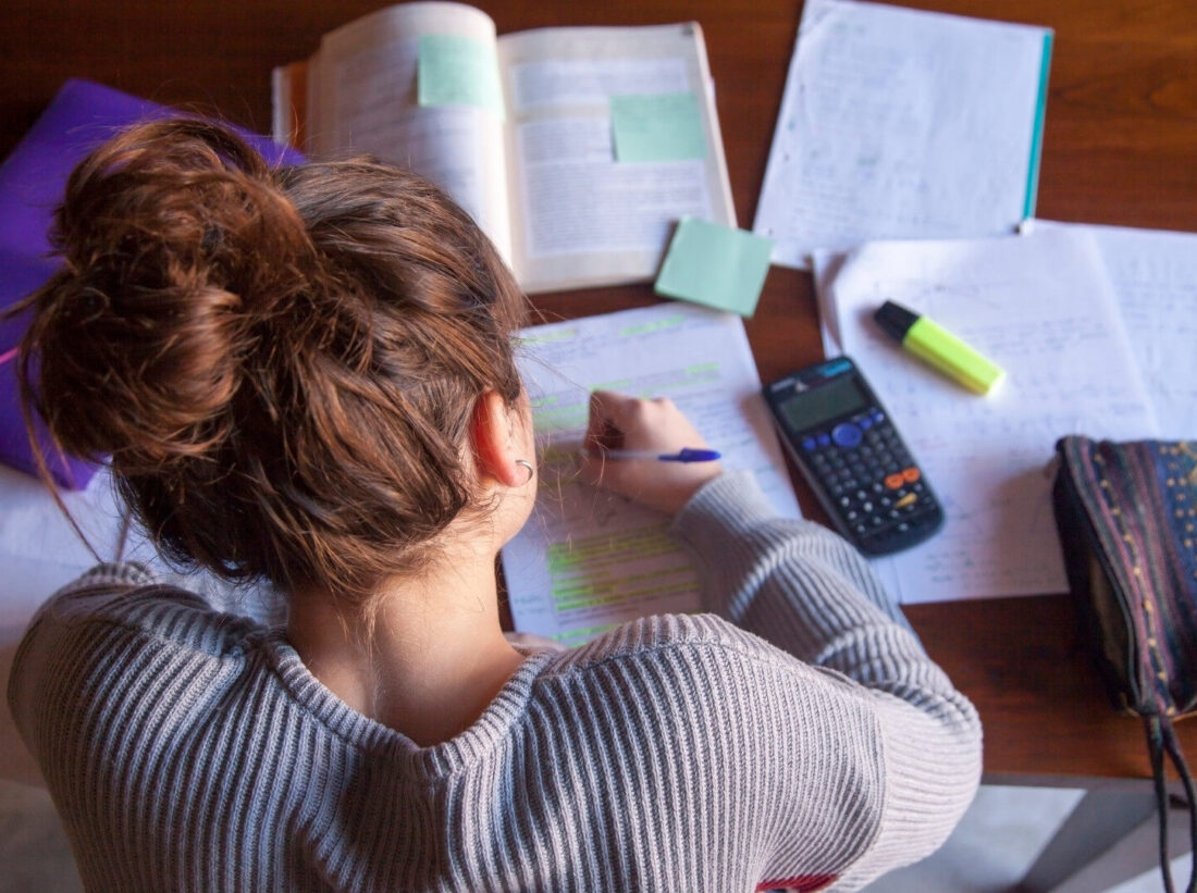 A teenage girl doing homework with various books and notes laid out on her desk A teenage girl doing homework with various books and notes laid out on her desk