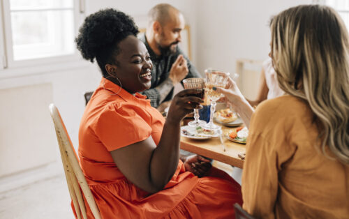 A side view of a smiling black female enjoying spending her leisure time with her diverse friends while holding a glass of wine.