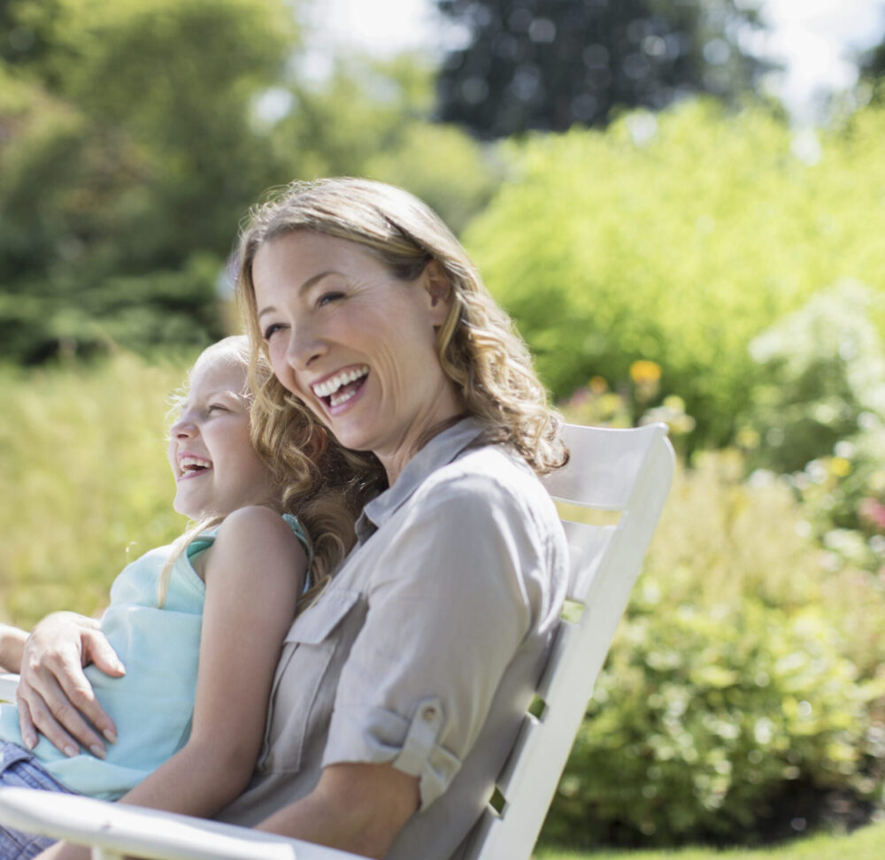 A woman sat on an outdoor chair with her daughter on her lap, smiling