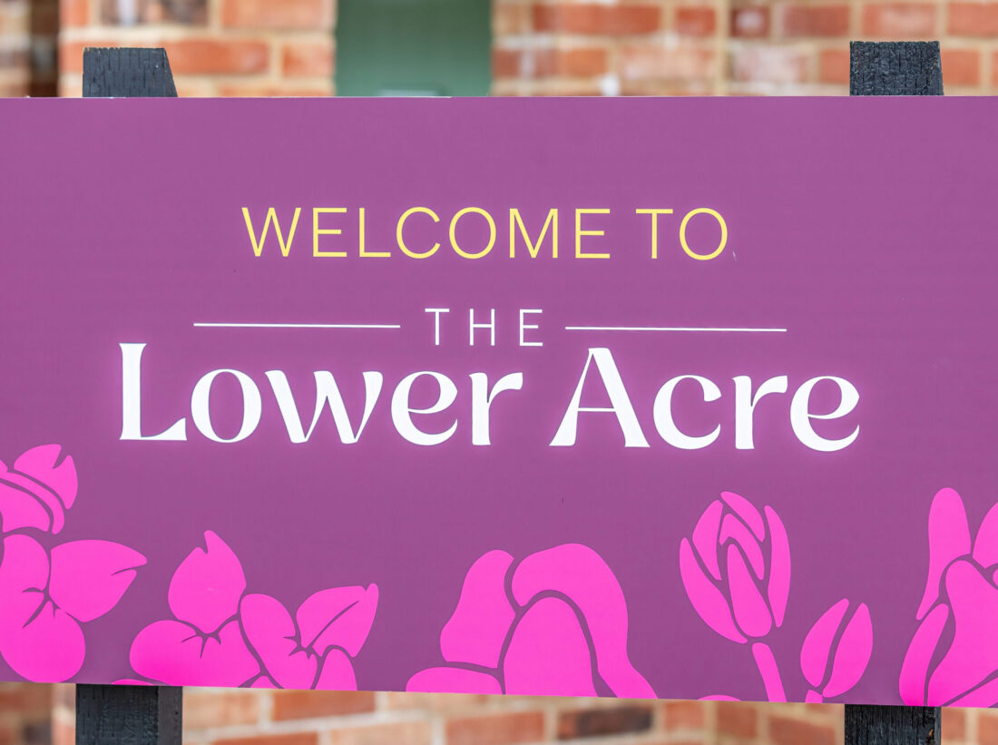 A purple sign reading 'Welcome to The Lower Acre' in front of a house