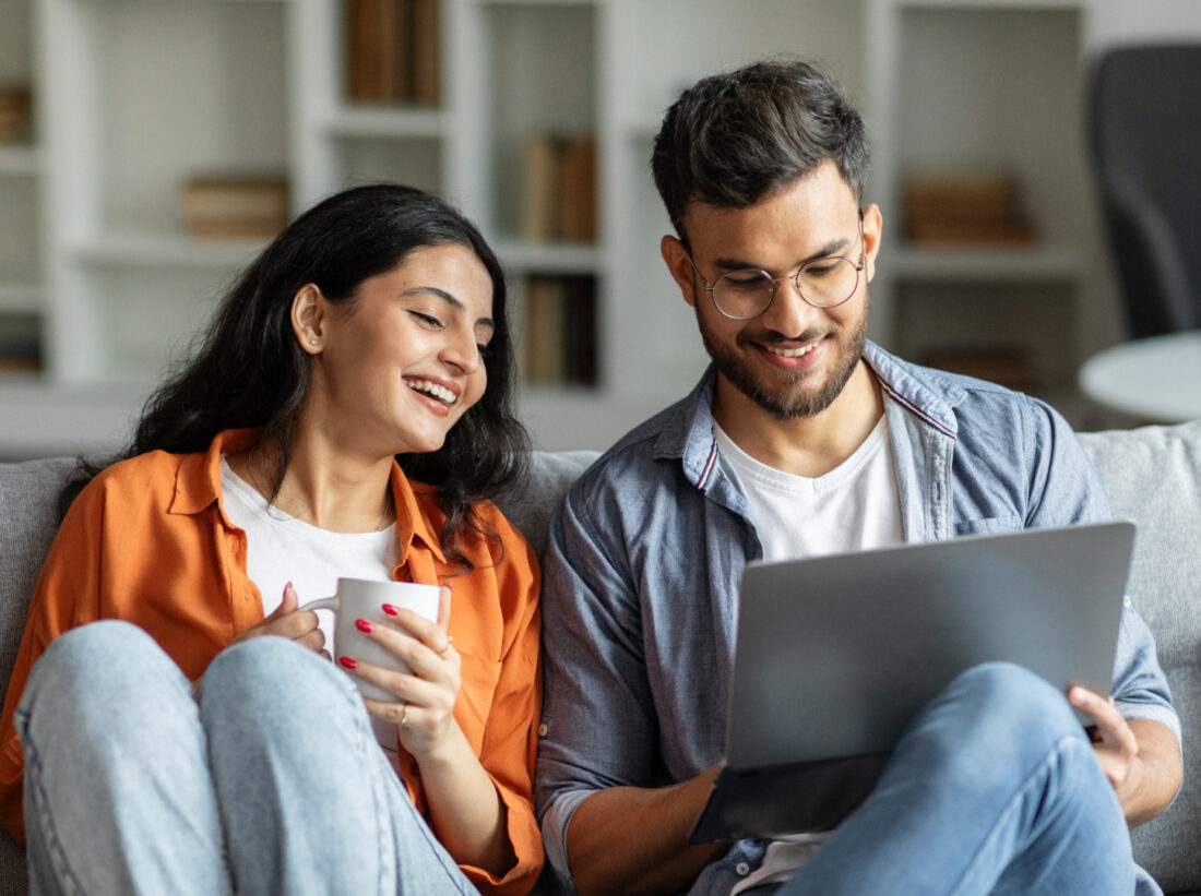A young couple sat of on sofa looking at a laptop